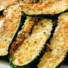 Fette di zucchine al forno, dorate e croccanti, con panatura e erbe aromatiche. Un contorno saporito e leggero.
