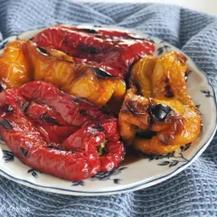 Piatto di peperoni arrostiti al forno, rossi e gialli, cotti alla perfezione, con un leggero velo di bruciatura che ne esalta il sapore.