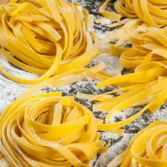 Nidi di tagliatelle fatte in casa, fresche e dorate, sparse su un piano cosparso di farina. Un invito alla tradizione culinaria.