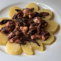 Un saporito polpo alla gallega, tagliato a pezzi e servito su fette di patate bollite, condito con erbe aromatiche.