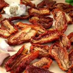 Pomodori secchi, aglio e basilico su un tagliere di legno. Un sapore intenso che evoca il sole e la terra.
