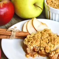 Un delizioso crumble di mele, con mele rosse e verdi sullo sfondo, cannella e fette di mela.