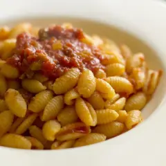 Un piatto di malloreddus alla campidanese, pasta sarda con sugo di pomodoro e salsiccia, serviti in una ciotola bianca.