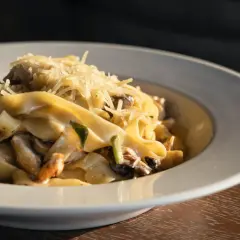 Un piatto di pasta fresca con salsiccia e funghi, condita con parmigiano grattugiato.