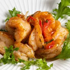 Gamberi sale e pepe succulenti, saltati con pomodorini e guarniti con insalata fresca su un piatto bianco texturizzato.