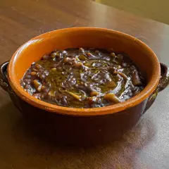 Una ciotola di terracotta piena di pasta e lenticchie, condita con olio d'oliva. Un piatto confortante e saporito.
