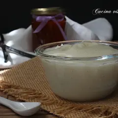 Una ciotola di cremosa crema al latte, profumata alla vaniglia, pronta per essere gustata. Accanto, un barattolo di marmellata e bacche di vaniglia.