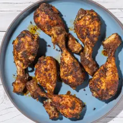 Cosce di pollo in friggitrice ad aria, dorate e succulente, servite su un piatto blu. Accanto, una ciotolina di senape.