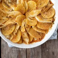 Finoçchi gratinati al forno, dorati e croccanti, in una pirofila bianca su un tavolo di legno.