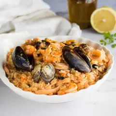 Un invitante risotto allo scoglio, ricco di cozze, vongole, gamberi e calamari, servito in una conchiglia bianca.