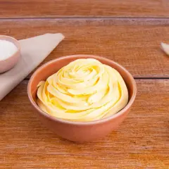 Una ciotola di soffice crema al burro, pronta per decorare torte. Accanto, ciotoline con zucchero e decorazioni naturali.