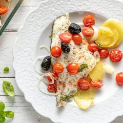 Filetti di orata al forno con pomodorini, olive nere e patate. Un piatto saporito e colorato, pronto per essere gustato.