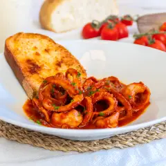 Un piatto di moscardini in umido, succulenti e profumati, accompagnati da una fetta di pane tostato e pomodorini freschi.