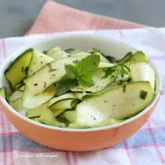 Insalata di zucchine marinate, condite con erbe aromatiche e menta fresca, servite in una ciotola di terracotta.
