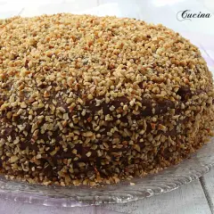 Torta ricoperta di cioccolato e nocciole tritate, una deliziosa pizza dolce abruzzese su un piatto di vetro.