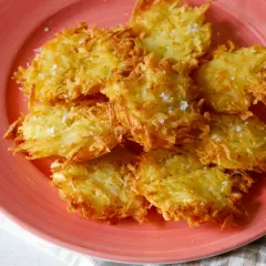 Tortel di patate dorati e croccanti, cosparsi di sale grosso, su un piatto rosa.