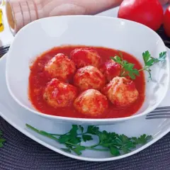 Polpette di merluzzo in salsa di pomodoro, guarnite con prezzemolo. Sullo sfondo, pomodori, cipolla e sale.