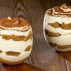Due bicchieri di tiramisù senza uova, stratificati con crema e savoiardi, spolverati di cacao.
