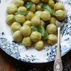 Un piatto di gnocchi di zucchine, conditi con burro e salvia, su un elegante piatto decorato.