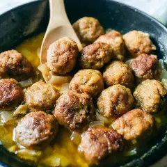 Polpette in bianco cremose in padella, dorate e succulente, adagiate su un letto di cipolle caramellate.