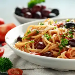Un piatto invitante di pasta alla puttanesca, con spaghetti conditi con pomodoro, olive nere e prezzemolo fresco.