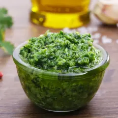 Una ciotola di fresca salsa verde, con ingredienti come aglio, pepe e olio d'oliva sullo sfondo.