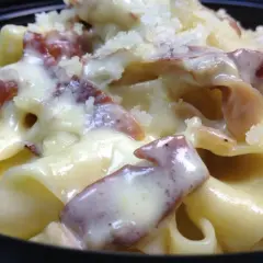 Primo piatto cremoso di pasta panna e speck, cosparso di formaggio grattugiato.
