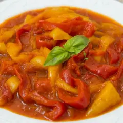 Peperonata ricetta della nonna: peperoni rossi e gialli stufati in un sugo saporito, guarniti con una fogliolina di basilico.