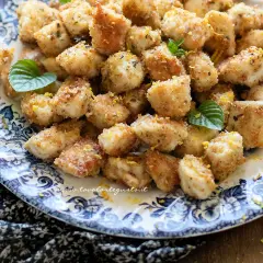 Bocconcini di pollo dorati e croccanti, guarniti con scorza di limone e foglioline di menta, serviti su un piatto decorato.