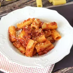 Piatto di rigatoni conditi con un sugo rosso piccante alla nduja, spolverati di parmigiano.