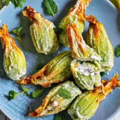 Fiori di zucca fritti, ripieni di formaggio cremoso e guarniti con menta fresca, su un piatto blu.