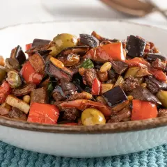 Un invitante piatto di caponata di verdure, con melanzane, peperoni rossi, olive verdi e capperi, pronto per essere gustato.