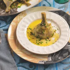 Un carciofo alla romana, tenero e profumato, servito su un piatto bianco con olio e prezzemolo.