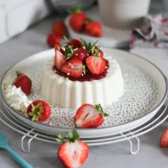 Deliziosa panna cotta con fragole fresche e salsa di fragole, guarnita con panna montata e foglioline di menta.