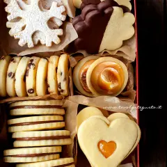 Scatola piena di biscotti al burro: a fiocco di neve, con gocce di cioccolato, ripieni di caramello e a forma di cuore.