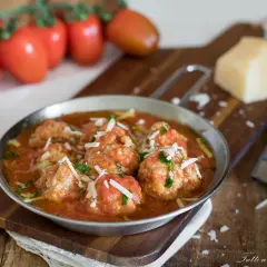 Polpette al sugo ricetta della nonna, succulente e profumate, servite in un piatto di metallo con pomodori freschi e parmigiano.