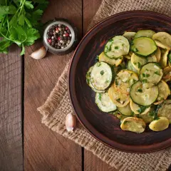 Piatto di zucchine trifolate, condite con aglio, prezzemolo e pepe, su un tavolo di legno rustico.