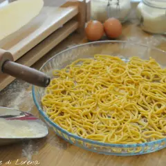 Spaghetti alla chitarra appena fatti, pronti per essere cucinati. Ingredienti freschi e attrezzi per la pasta sul tavolo.