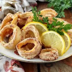 Anelli di calamari gratinati al forno, dorati e croccanti, guarniti con spicchi di limone e prezzemolo fresco.
