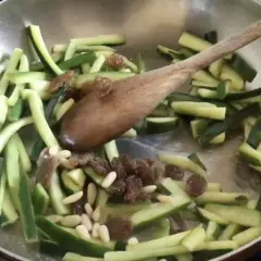 Zucchine tagliate a julienne con uvetta e pinoli in padella, pronte per essere trasformate in un delizioso piatto agrodolce.