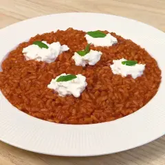 Un cremoso risotto al pomodoro, arricchito da ciuffi di ricotta fresca e basilico, servito su un piatto bianco.