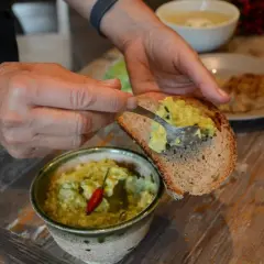 Mani che spalmano la salsa guacamole ricetta su una fetta di pane tostato. Un peperoncino rosso decora la ciotola.
