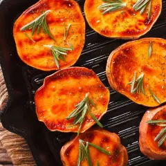 Fette di patate dolci grigliate in padella con rosmarino e spezie, pronte per essere gustate.