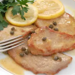 Scaloppine al limone cremose, guarnite con capperi, prezzemolo e fette di limone, pronte per essere gustate con una forchetta.