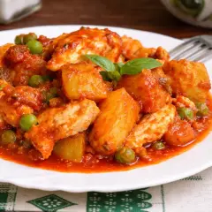 Un saporito spezzatino di pollo con patate e piselli in salsa rossa, guarnito con basilico fresco.
