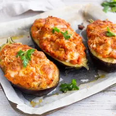 Melanzane ripiene al forno velocissime, dorate e filanti, guarnite con prezzemolo fresco su una teglia.