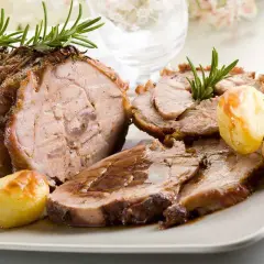 Succulento arrosto di vitello affettato, guarnito con rosmarino e accompagnato da patate arrosto dorate.