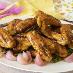 Alette di pollo dorate e succulente, servite con cipolle rosse e asparagi su un piatto bianco.