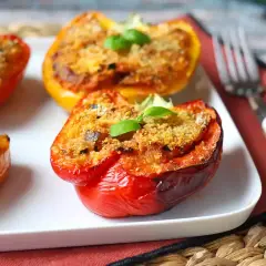 Peperoni ripieni al forno, colorati e invitanti, con un ripieno dorato e una fogliolina di basilico fresco.