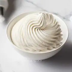 Una ciotola bianca piena di soffice crema chantilly, con striature perfette e puntini di vaniglia visibili.